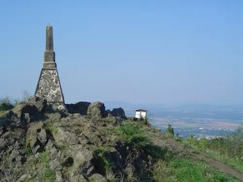 Kamenný pomník na skalnatém vrcholu s výhledem do krajiny.