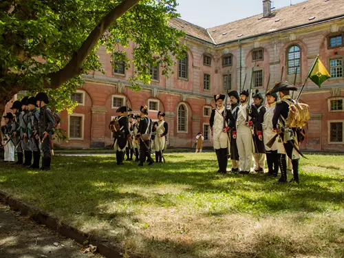 Skupina historických rekonstruktérů v uniformách stojí na trávníku před palácem.