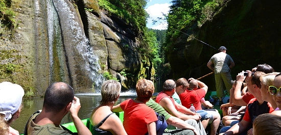 Turisté v lodi plavou Divokými soutěžkami u vodopádu.