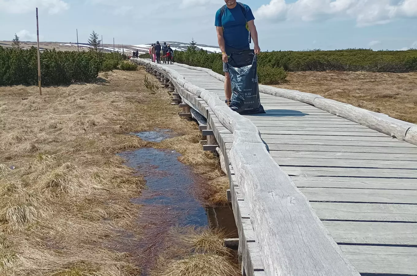 Turista s pytlem na odpadku kráčí po dřevěné chodníčku v Peči pod Sněžkou.