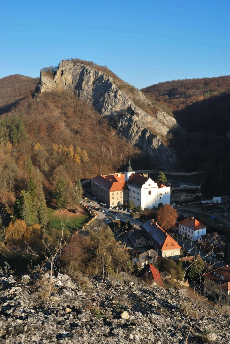 Zámek v kopcovité krajině s lesy pod modrou oblohou.
