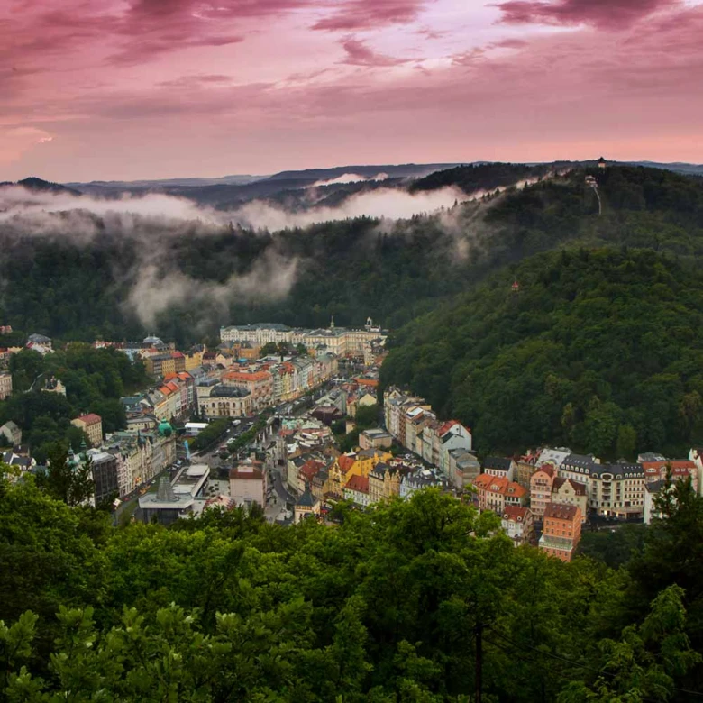 Pohled na městečko Karlovy Vary obklopené horami s mlhou.